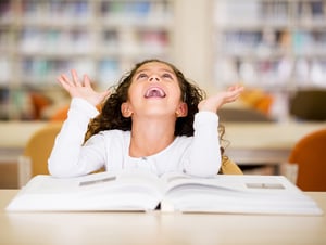 Excited schoolgirl at the library reading a book